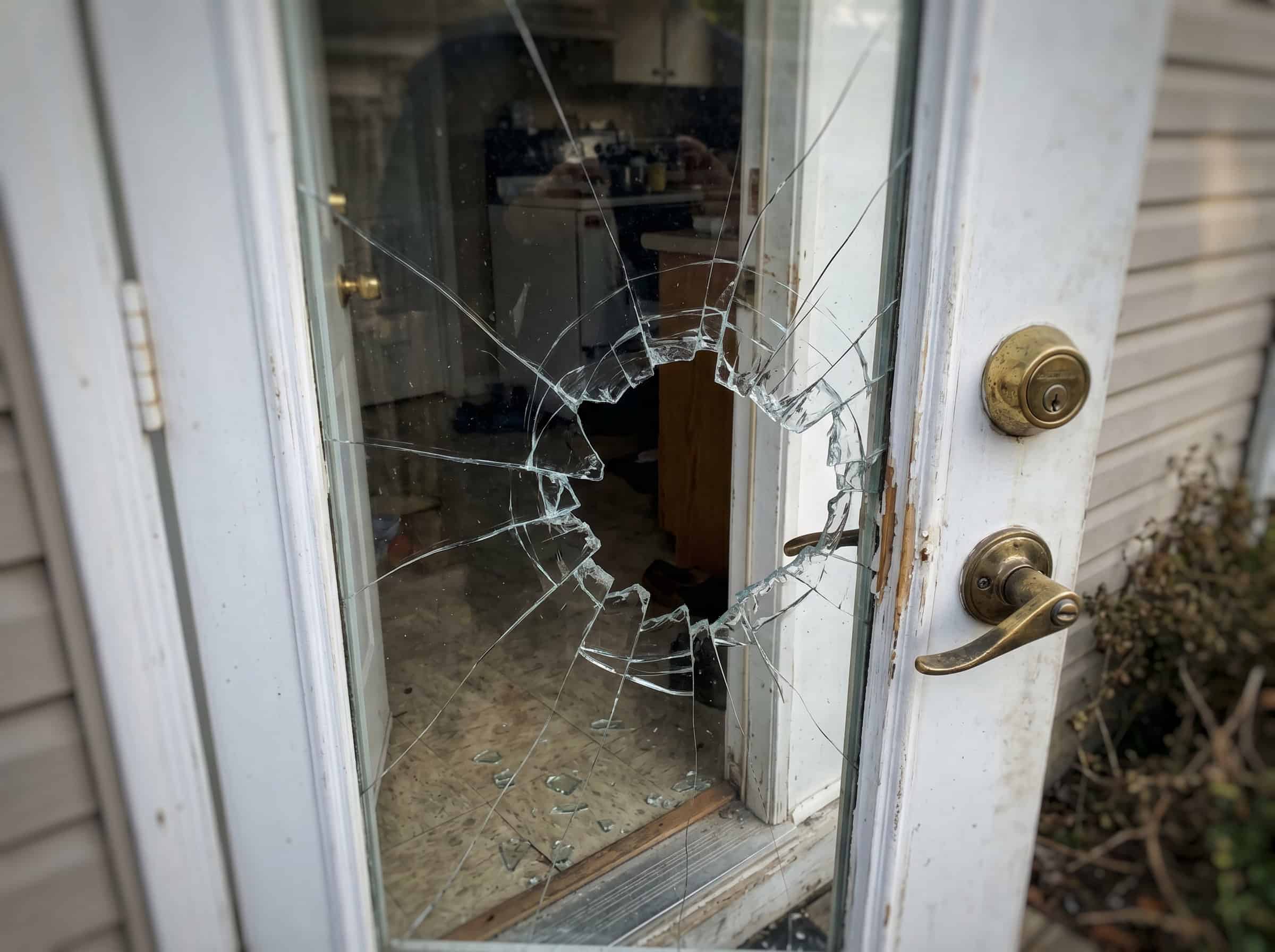 Real job photo: a hole smashed through back door glass right beside the deadbolt, the kitchen visible through the broken pane