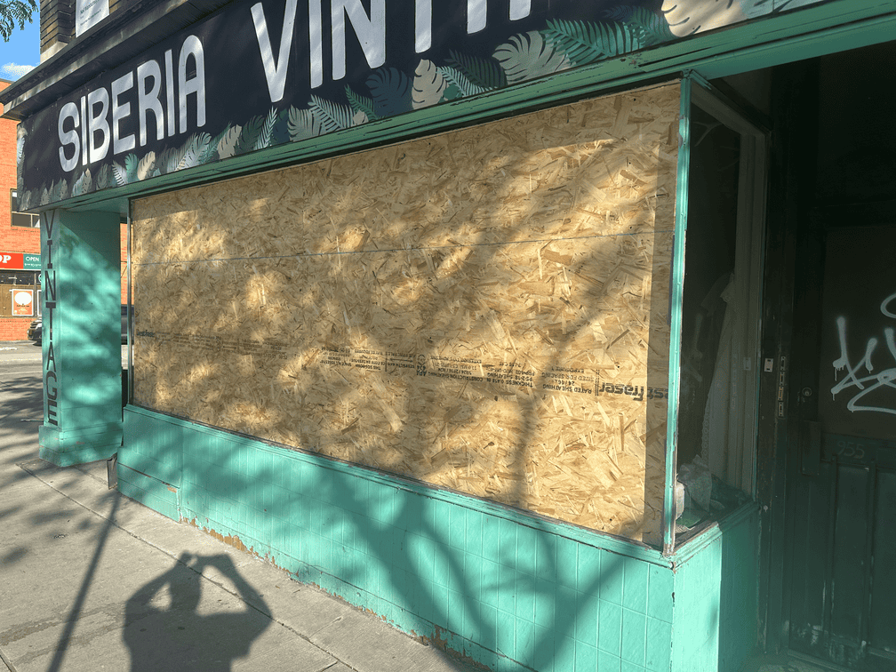 A storefront opening closed off with a solid board, secured against re-entry while the glass is sorted.