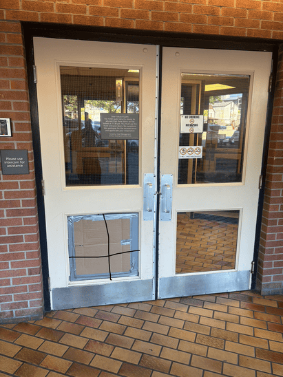 A commercial entry door with the broken lower panel covered and locked down.