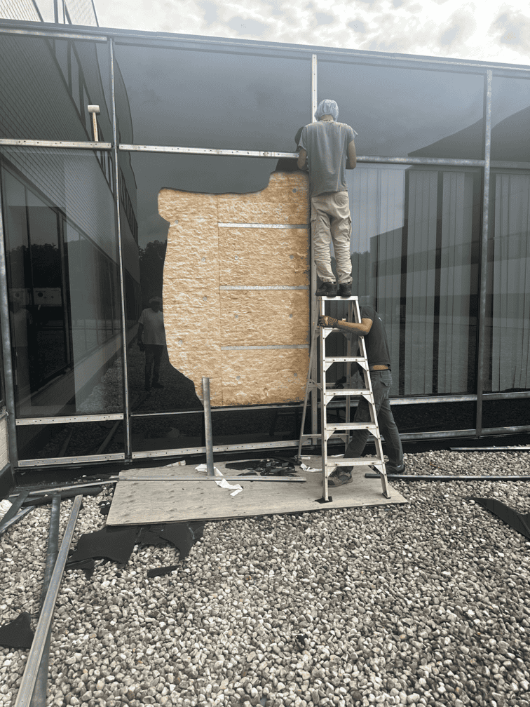 A Glass 911 crew member on a ladder boarding up a damaged storefront opening on site.