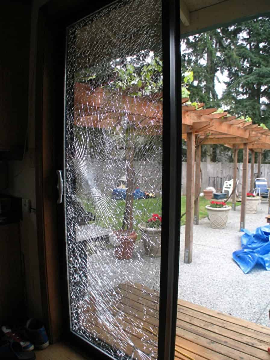 Real job photo: a sliding patio door pane crazed by an impact, the backyard pergola visible through the cracks