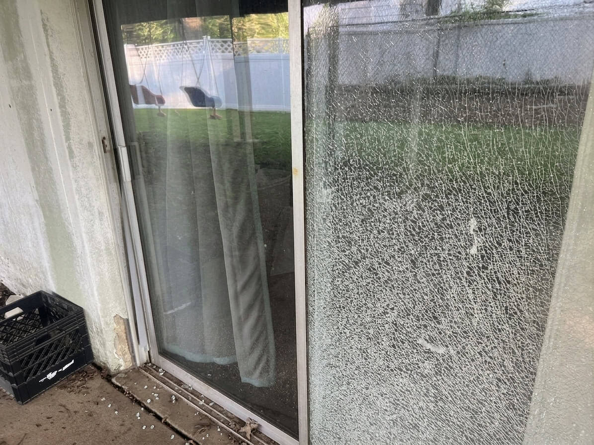 Real job photo: a sliding patio door pane shattered into tempered crumbs, the backyard fence behind it, broken glass on the back step