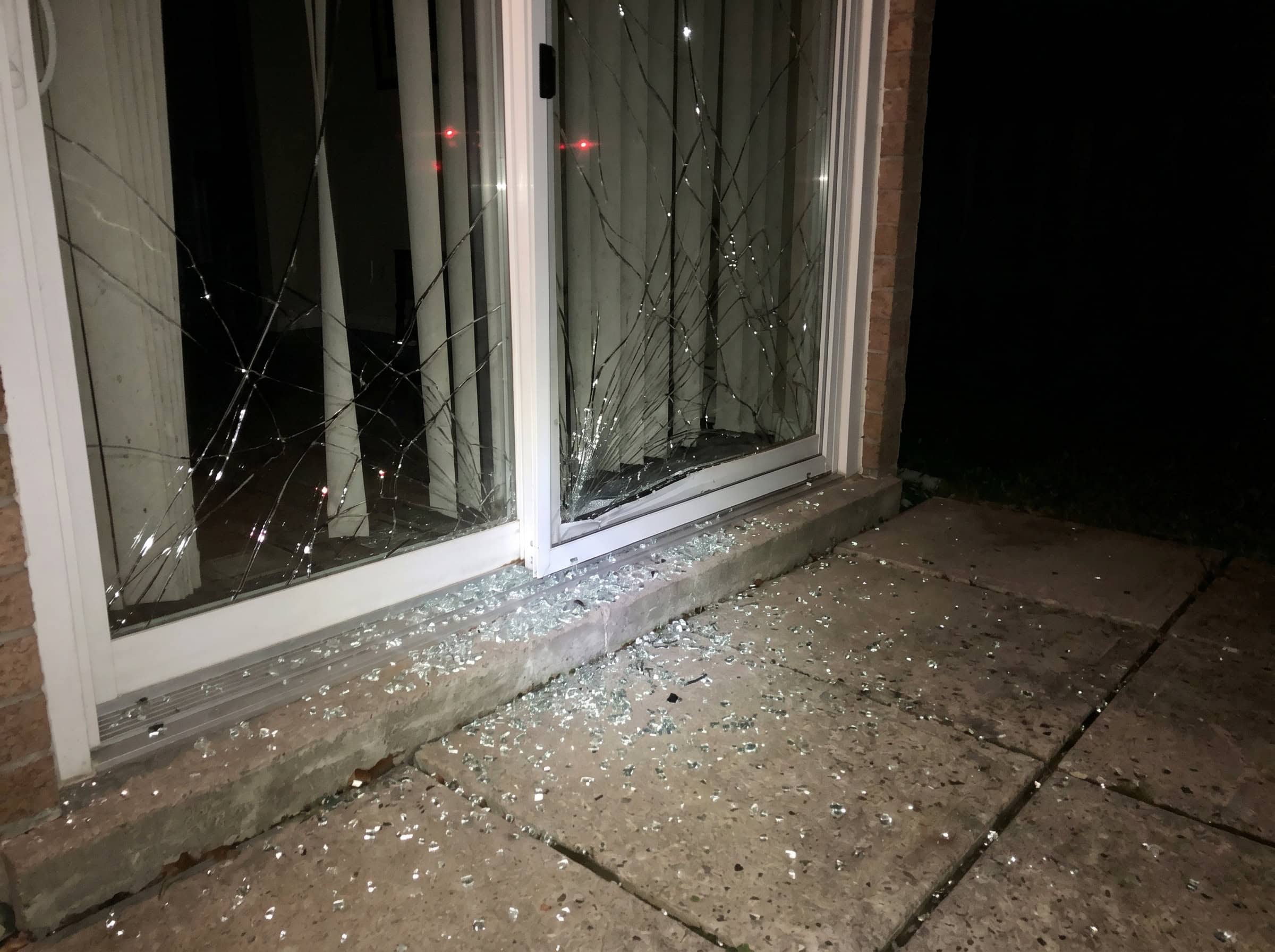 Real job photo: a patio slider crazed after a night break-in, shot by phone flash, broken glass scattered across the patio stones